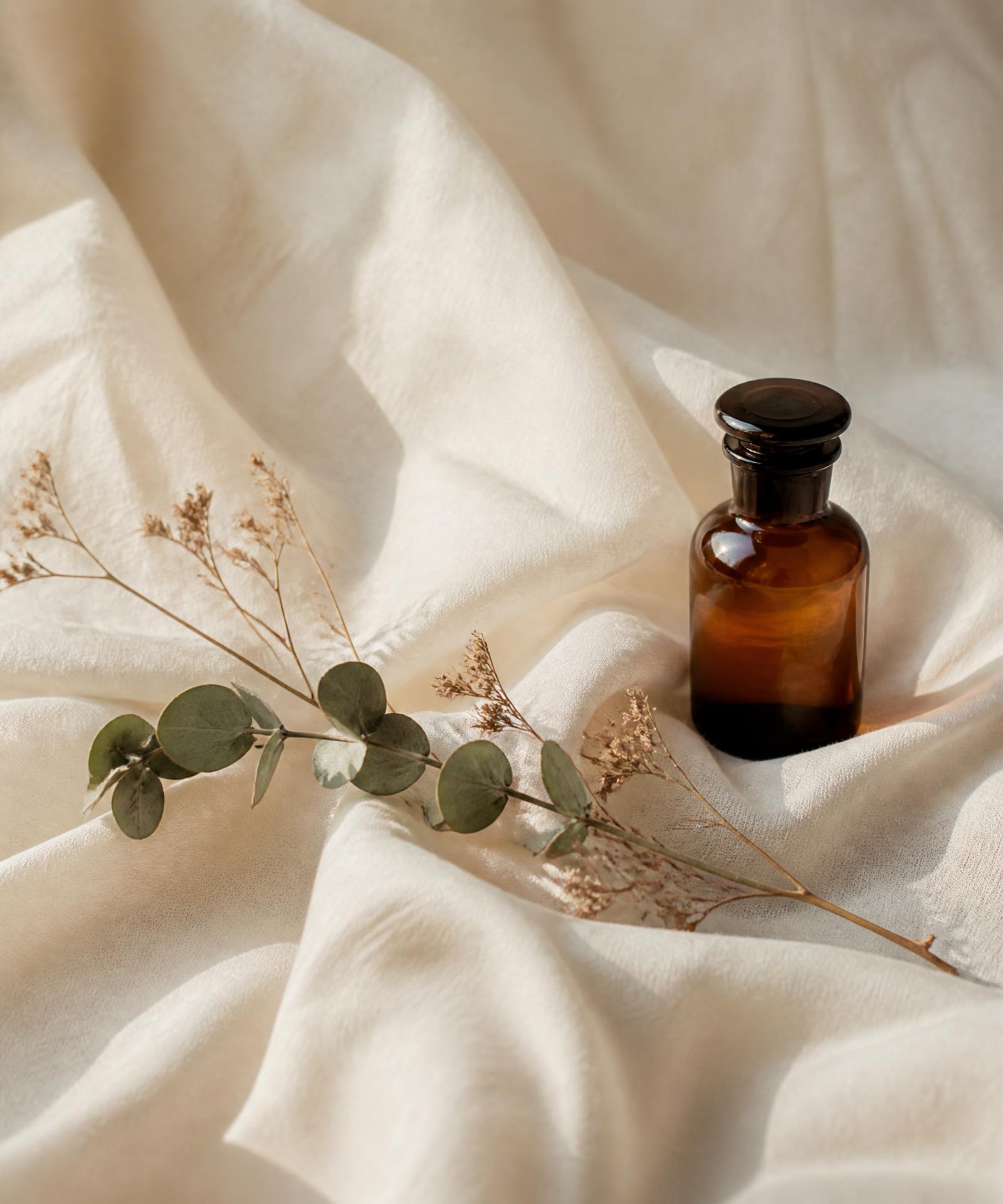 Soft botanical still life with amber apothecary bottle on draped ivory linen